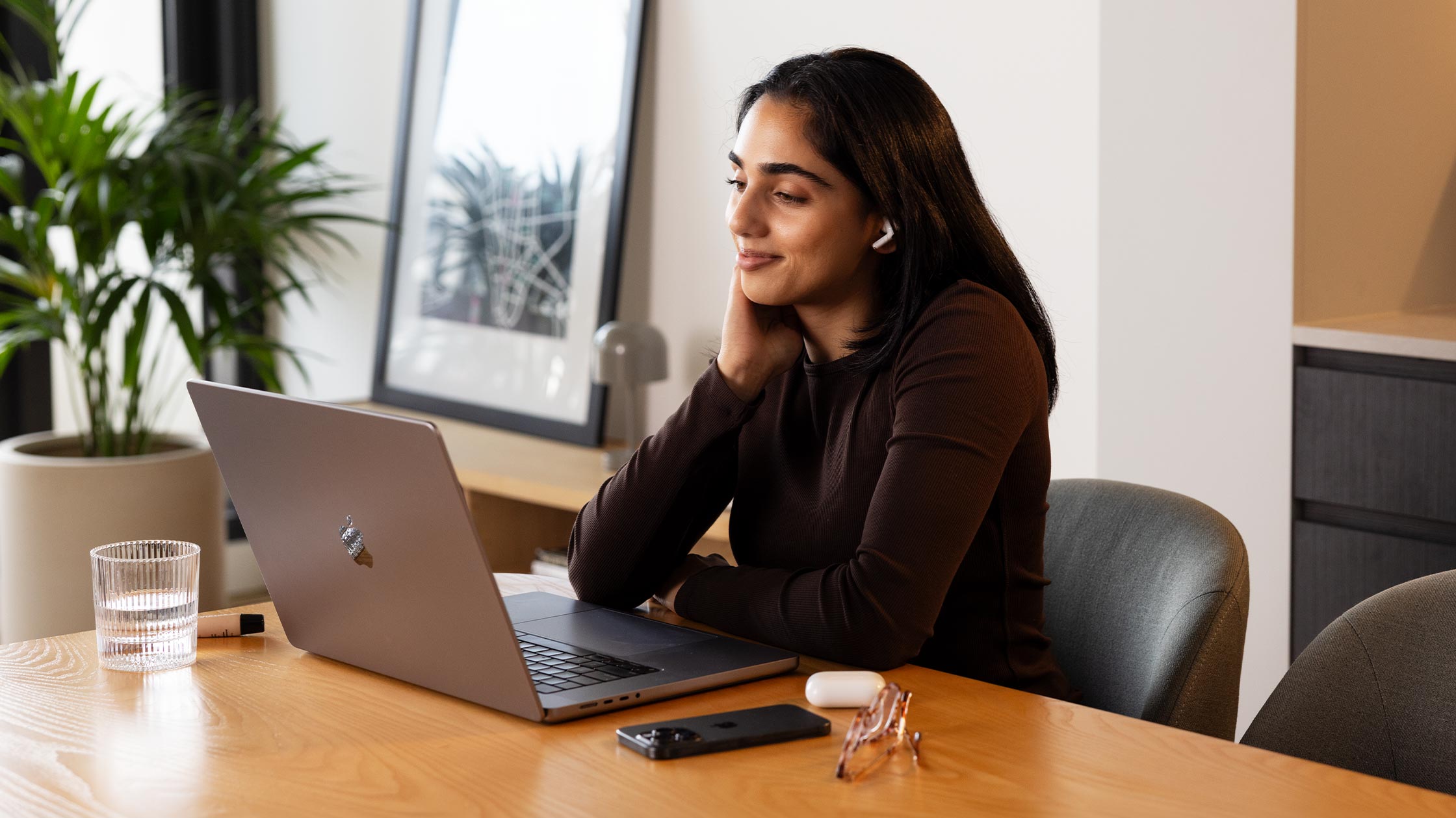 A woman talks to someone through her earphones as she looks at her laptop.