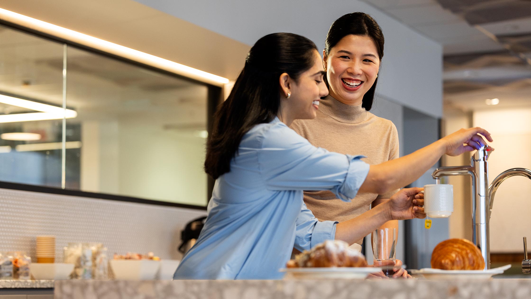 Two females chat in the kitchen while making a cup of tea.