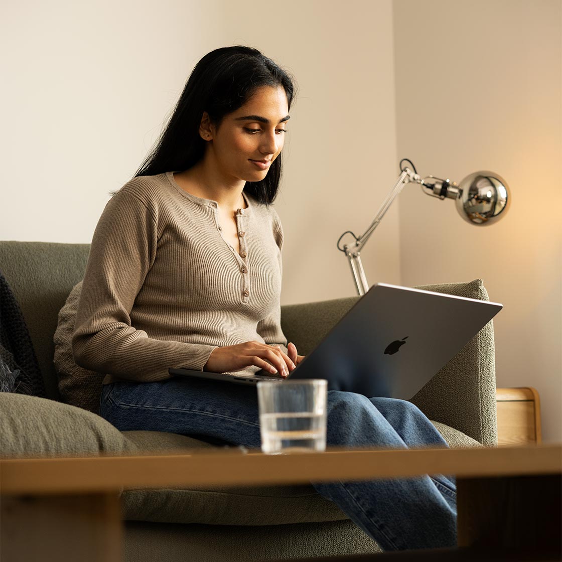 A young woman sits on her couch at home looking at her laptop.