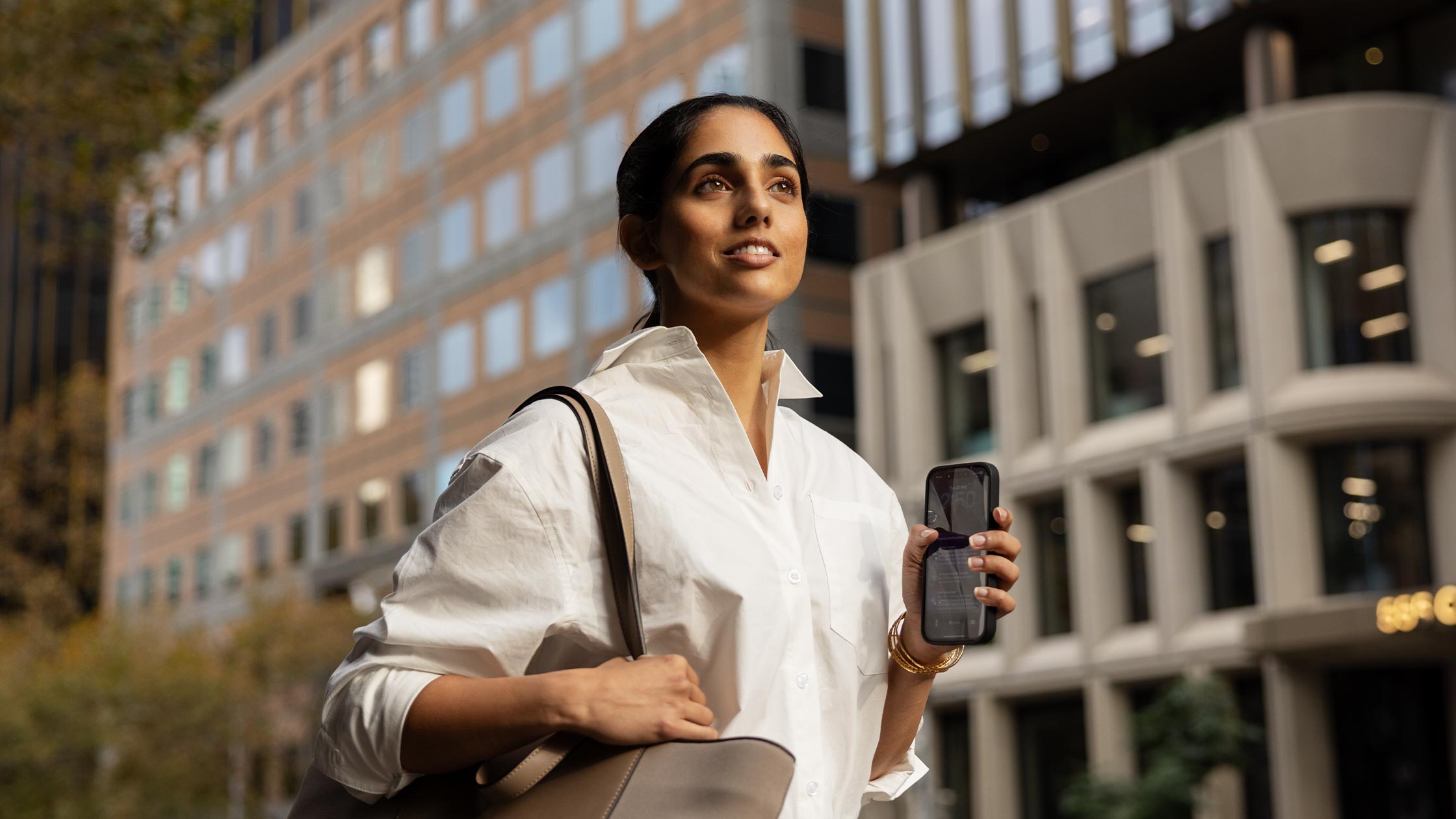 A young woman walks through the city. She is smiling confidently.