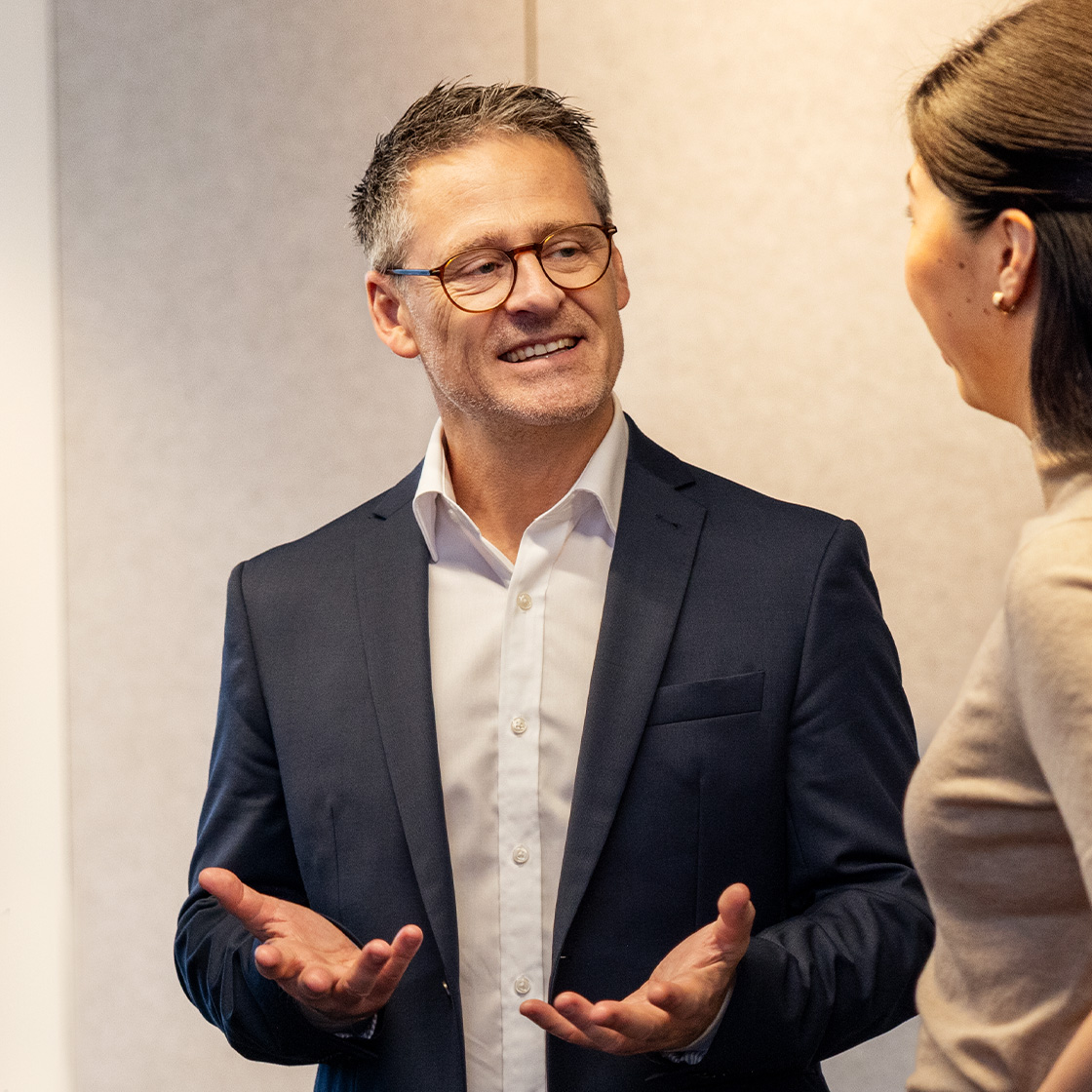 A man stands proudly looking to the right, talking to a woman.