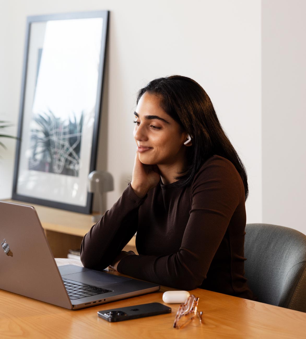A woman talks to someone through her earphones as she looks at her laptop.