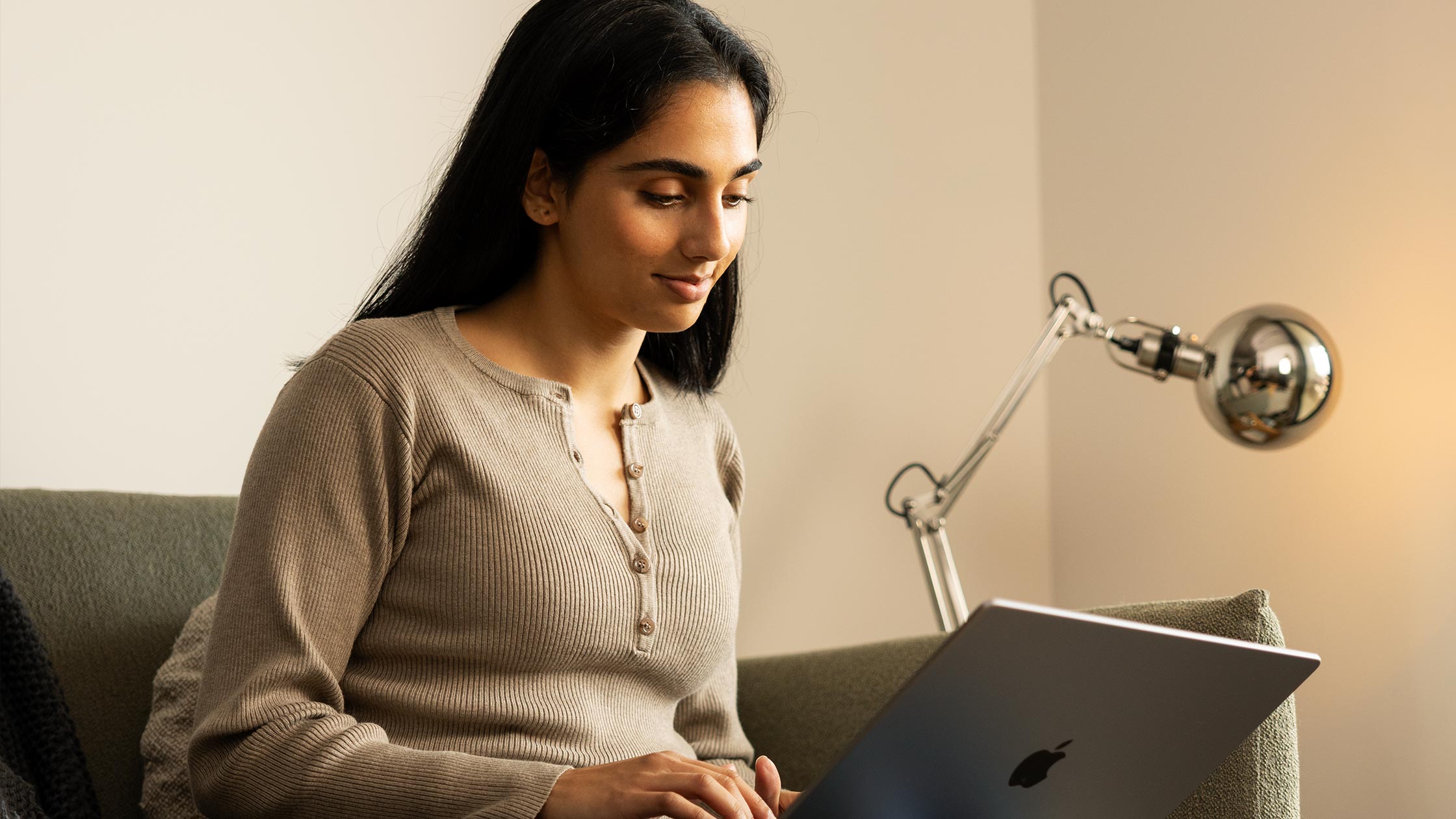 A young woman sits on her couch at home looking at her laptop.